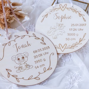 May include: Two wooden baby announcement plaques with decorative floral borders. One plaque features a unicorn and the name "Sophie" with birth details: 25.01.2017, 17:26 Uhr, 3000 g, 50 cm. The other plaque features a tiger and the name "Jonah" with birth details: 08.03.2023, 20:08 Uhr, 3950 g, 54 cm.
