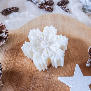 May include: A white snowflake-shaped candle on a wooden surface. The candle has a detailed design and a white wick.