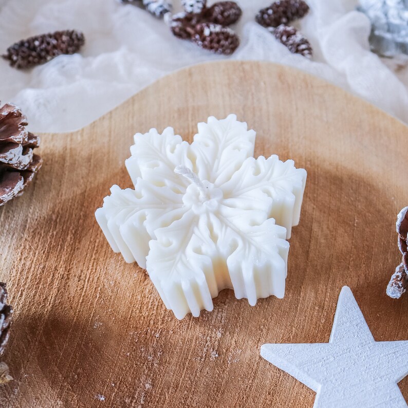 May include: A white snowflake-shaped candle on a wooden surface. The candle has a detailed design and a white wick.