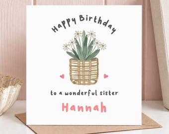 May include: A square greeting card with a white background featuring a watercolor illustration of a potted plant in a woven basket. The text reads Happy Birthday to a wonderful sister Hannah in dark gray and pink, with two small pink hearts.