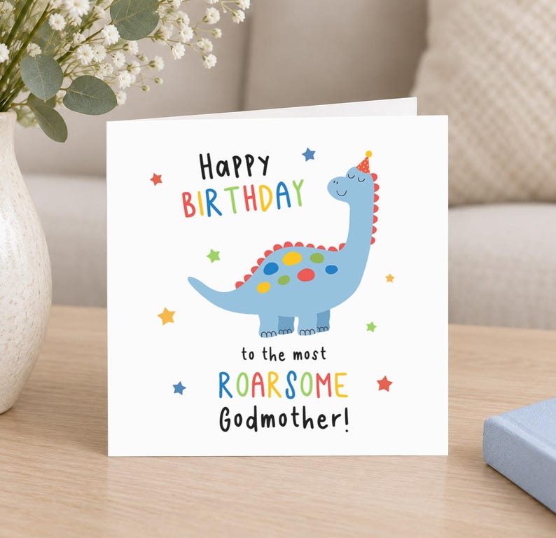 Op de afbeelding: Een vierkante witte wenskaart met een blauwe dinosaurus die een feesthoedje draagt. De tekst luidt Happy Birthday to the most ROARSOME Godmother! Het ontwerp bevat kleurrijke stippen op de dinosaurus en kleine sterretjes.
