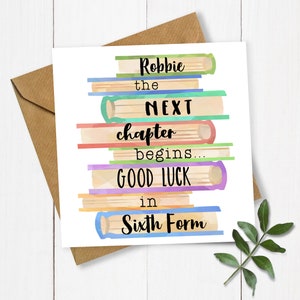 May include: A square greeting card featuring a stack of colourful watercolour books. The text reads "Robbie the NEXT chapter begins... GOOD LUCK in Sixth Form". The card is accompanied by a brown envelope and a sprig of greenery.