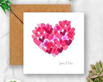 May include: A white card with a pink heart made of smaller pink hearts. The text "James & Fiona" is written at the bottom of the card.