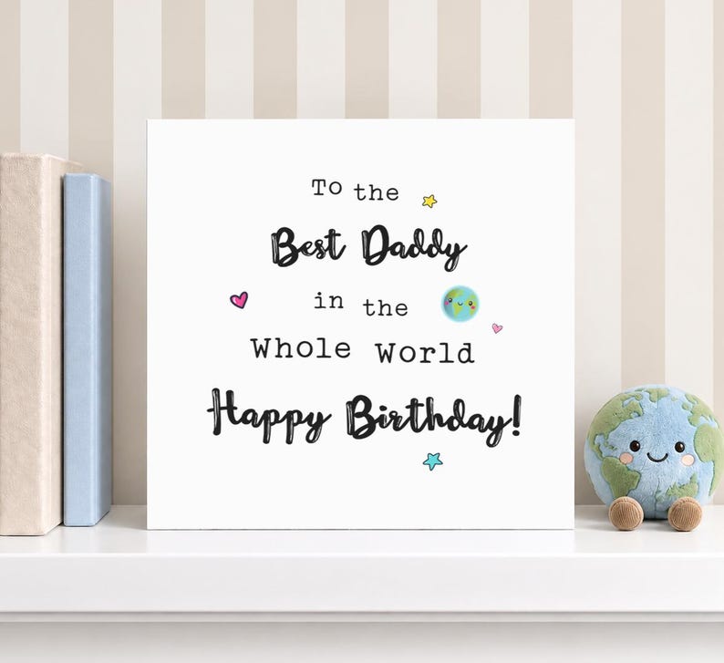 May include: A square white greeting card with black text that reads To the Best Daddy in the Whole World Happy Birthday. The card features small colorful illustrations of a smiling planet Earth, a pink heart, and yellow and blue stars.
