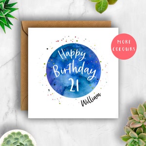 Op de afbeelding: Een witte kaart met een blauwe waterverf cirkel met de tekst "Happy Birthday 21 William" in wit. De cirkel is omringd door kleurrijk confetti.