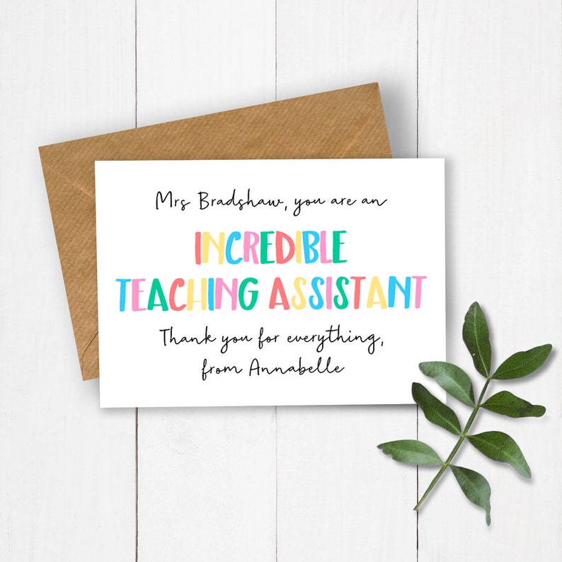 Op de afbeelding: Een witte wenskaart met de tekst "Mrs Bradshaw, you are an INCREDIBLE TEACHING ASSISTANT" in kleurrijke letters. Naast de kaart ligt een bruine envelop en een groene tak.