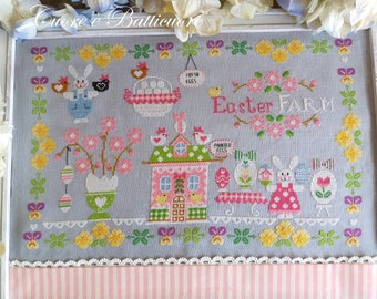 May include: Cross-stitch embroidery featuring a pastel-colored Easter farm scene with a pink house, a bunny holding a basket of eggs, and a sign that reads "Easter Farm".