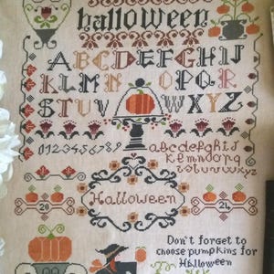 Op de afbeelding: Borduurpatroon met een Halloween-thema met een heks, pompoenen en de woorden "Halloween" en "Vergeet niet om pompoenen te kiezen voor Halloween".