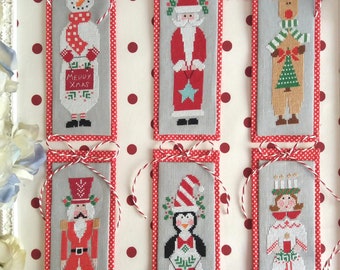May include: Six Christmas-themed cross-stitch ornaments with red and white polka dot borders. The ornaments feature a snowman, Santa Claus, a reindeer, a nutcracker, a penguin, and a girl with candles.