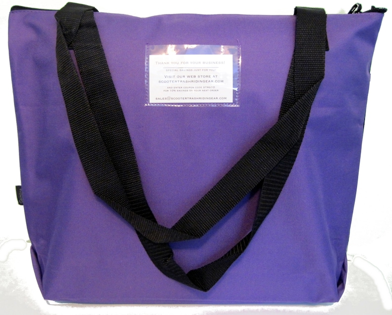 May include: A purple tote bag with black straps. The bag has a rectangular clear pocket with white text. The bag has a zipper closure at the top. The straps are sewn to the bag and extend down the sides.