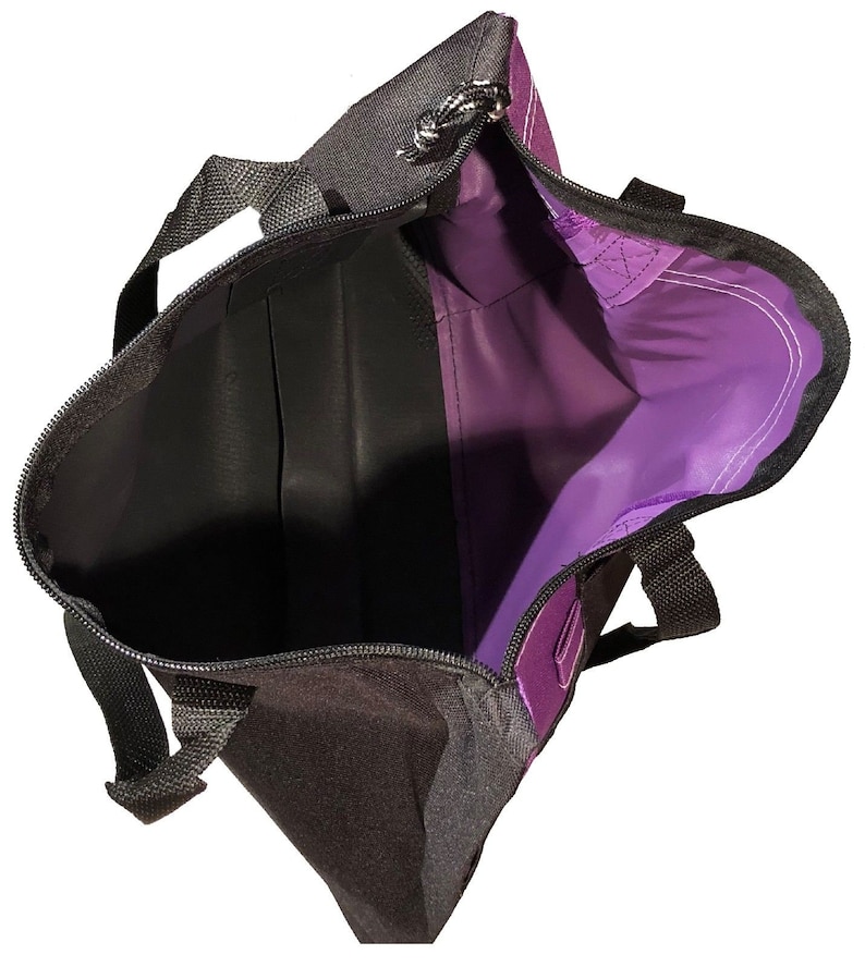 May include: A purple and black tote bag with a zipper closure and two handles. The bag is open and the inside is visible.