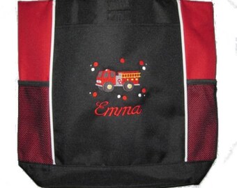 May include: Black tote bag with red side panels and a white zipper. The bag has a mesh pocket on each side. The front of the bag features an embroidered red fire truck with the name "Emma" underneath.
