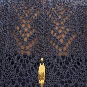 May include: A gold-toned, hammered metal fish pendant suspended from a thin black cord. The pendant features a smooth, reflective surface with a textured, dimpled finish, hanging vertically from a small gold bead at the top of the cord.