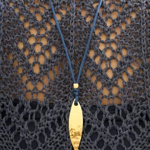May include: A gold-toned fish-shaped pendant with a hammered texture, suspended from a thin blue cord. The pendant features a smooth, reflective surface with subtle indentations, attached to the cord by a small gold-colored metal bead.