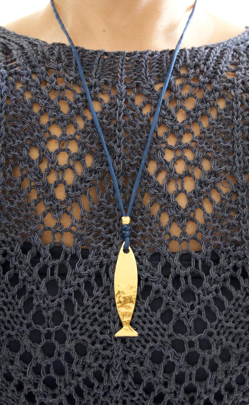 May include: A gold-toned fish-shaped pendant with a hammered texture, suspended from a thin blue cord. The pendant features a smooth, reflective surface with subtle indentations, attached to the cord by a small gold-colored metal bead.