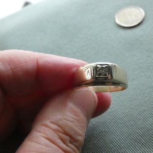 May include: A gold band ring with a single, square-cut diamond in the centre.