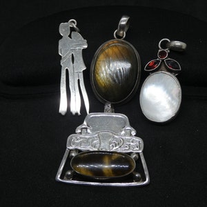 May include: Four silver pendants with different stones. One pendant features a couple embracing, another has a brown and black stone, a third has a gold and black stone, and the last has a white stone with red accents.