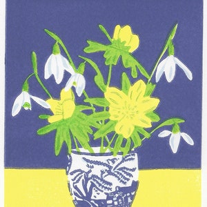 Op de afbeelding: Een blauwe en witte porseleinen vaas met een bloemenmotief bevat een boeket witte sneeuwklokjes en gele winterakonietbloemen. De vaas staat op een gele ondergrond tegen een paarse achtergrond. De tekst "Winter Eggcup. 1/50." is onder de vaas gedrukt.