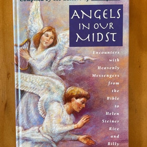 Peut inclure: Livre intitulé "ANGELS IN OUR MIDST" avec des illustrations d'anges. La couverture présente un carré bleu avec du texte blanc et la phrase "Rencontres avec des messagers célestes". Le livre est compilé par les éditeurs de Guideposts.