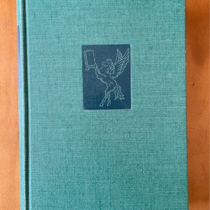 Könnte beinhalten: Ein grünes Hardcover-Buch mit einer Schwarzweißillustration eines geflügelten Pferdes, das ein Buch auf dem Einband hält.