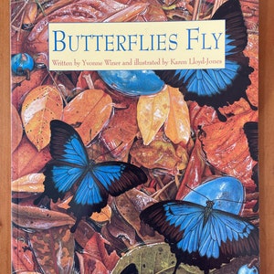 Puede incluir: Una portada de libro con el título "Butterflies Fly" escrito en letras amarillas. La portada presenta una ilustración colorida de dos mariposas azules con alas negras sobre un fondo de hojas marrones y naranjas.