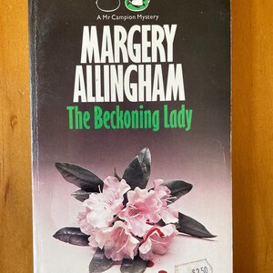 Puede incluir: Una portada de libro de bolsillo con fondo negro y texto blanco. El título es "Margery Allingham The Beckoning Lady". La portada presenta una flor rosa con gotas de sangre sobre un fondo blanco.