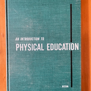 Puede incluir: Un libro de tapa dura verde con el título "An Introduction to Physical Education" y el nombre del autor "Nixon" impreso en la portada.