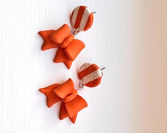 May include: A pair of orange bow earrings with white and orange striped circle accents.