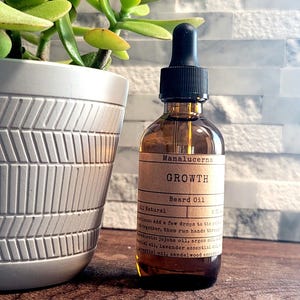 May include: A brown glass bottle of beard oil with a black dropper, labeled "GROWTH." The bottle sits on a wooden surface next to a white patterned pot with a green plant. The background is a white and gray tiled wall.