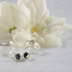 May include: Two silver wire ear cuffs with black and blue rhinestones. The ear cuffs are labeled "Jet Hematite" and "Jet #13".
