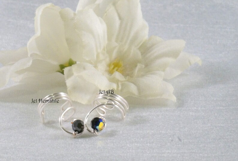 May include: Two silver wire ear cuffs with black and blue rhinestones. The ear cuffs are labeled "Jet Hematite" and "Jet #13".