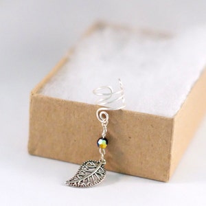 May include: Silver ear cuff with a spiral design and a dangling leaf charm. The charm is attached to a silver chain with a single iridescent bead.