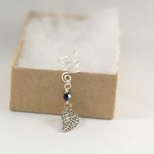 May include: Silver ear cuff with a spiral design and a dangling leaf charm. A black bead hangs above the leaf.
