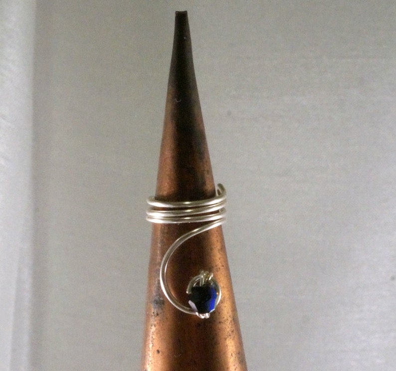 May include: A silver wire ring with a blue iridescent gemstone. The ring is displayed on a brown cone-shaped ring holder.
