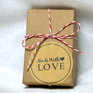 May include: A small brown box tied with red and white twine. A round sticker with the text "Made With LOVE" is attached to the box.