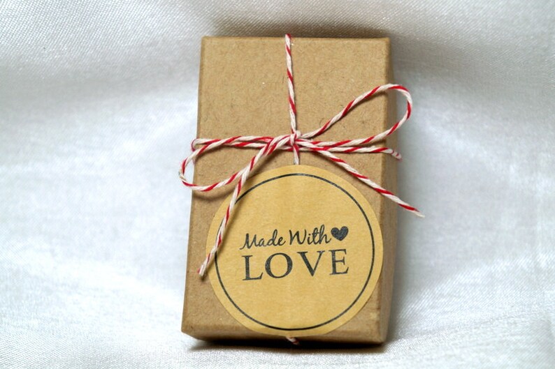 May include: A small brown box tied with red and white twine. A round sticker with the text "Made With LOVE" is attached to the box.