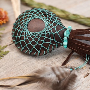 May include: A brown leather pouch with a turquoise beaded fringe and a turquoise net design. The pouch is decorated with turquoise beads and has a brown leather tassel.