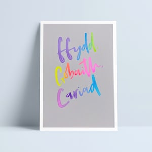 Puede incluir: Un fondo gris con las palabras galesas "ffydd", "gobaith" y "cariad" escritas en colores arcoíris.
