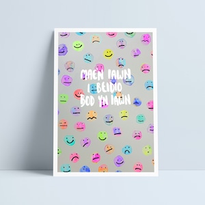 Puede incluir: Un fondo gris claro con un patrón de caras sonrientes de colores. El texto "mae'n iawn i berdio bod yn iawn" está escrito en blanco en el centro de la imagen.