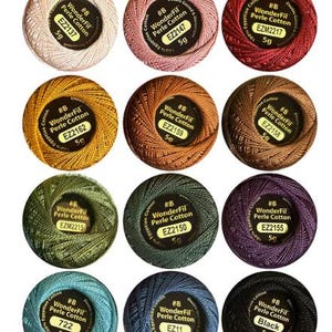 May include: Twelve round balls of WonderFil Perle Cotton thread in various colors, each labeled #8, 5g, and 100% Egyptian Cotton. The colors include cream, pink, red, gold, copper, brown, olive green, forest green, purple, teal, blue, and black.