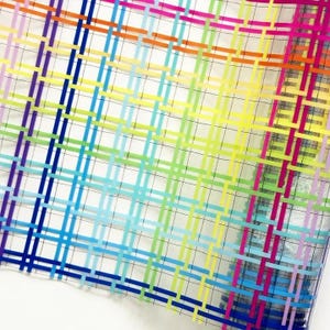 May include: A roll of semi-transparent mesh fabric featuring a vibrant rainbow-colored grid pattern. The design consists of intersecting horizontal and vertical lines in shades of red, orange, yellow, green, blue, and purple, creating a woven effect.