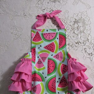 May include: A pink and green watermelon print baby onesie with a pink ruffled trim around the legs. The onesie has a halter top with a bow at the neck.