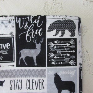 May include: Black and white fabric with a patchwork design featuring animals, arrows, and inspirational text. The text includes "wild & free", "be brave", "stay clever", and "be yourself".