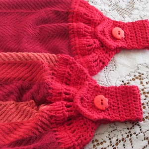 May include: Red and orange striped kitchen towel with crocheted red loops and red buttons.