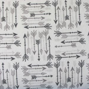 May include: A white fabric with a repeating pattern of black and gray arrows. The arrows are pointing in different directions and have a simple, geometric design.