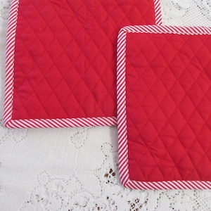 May include: Two red quilted pot holders with white and red striped trim.