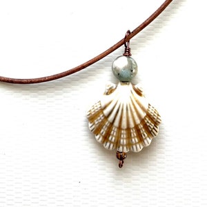 May include: A brown leather cord necklace with a white seashell pendant and a small blue bead. The seashell has a gold-colored pattern.
