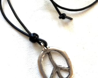 May include: A silver-colored peace sign pendant necklace with a black cord. The pendant is oval-shaped with a peace symbol in the center. The cord is adjustable with a sliding knot.