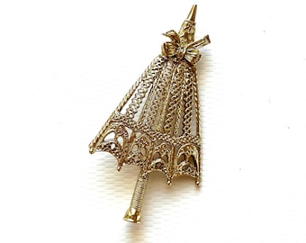 May include: A gold-toned filigree umbrella brooch with a bow at the top.