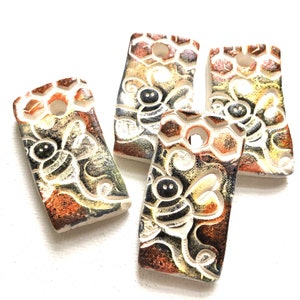 May include: Four ceramic bee-themed tiles with a honeycomb pattern and a hole in the center. The tiles are painted in shades of brown, yellow, and black.